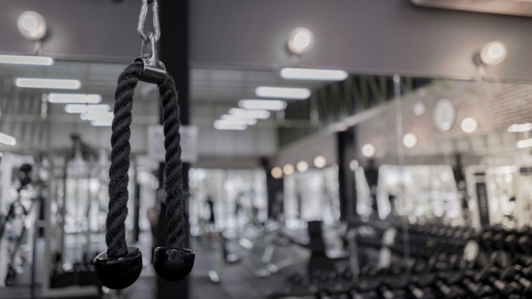 A triceps rope hangs on a cable machine in an empty gym.