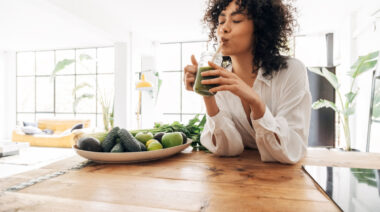 A person sips on a green juice in their kitchen.