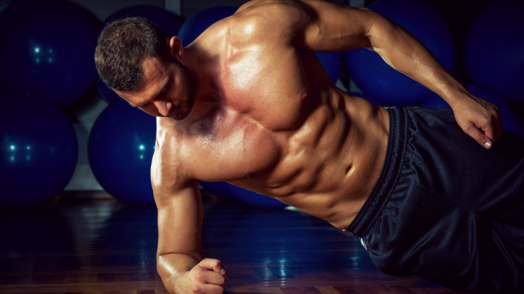 A shirtless person holds a side plank in the gym.