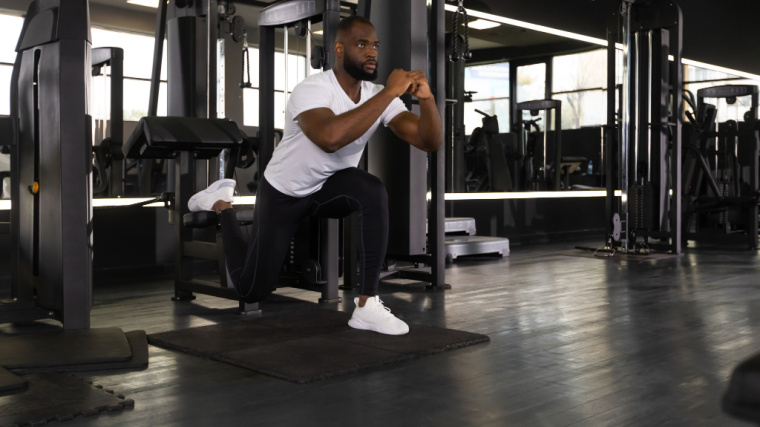 A person performs a Bulgarian split squat in the gym.