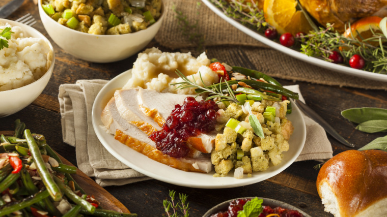 A plate on a packed table is full of food, including slices of turkey, cranberry sauce, mashed potatoes, and stuffing.