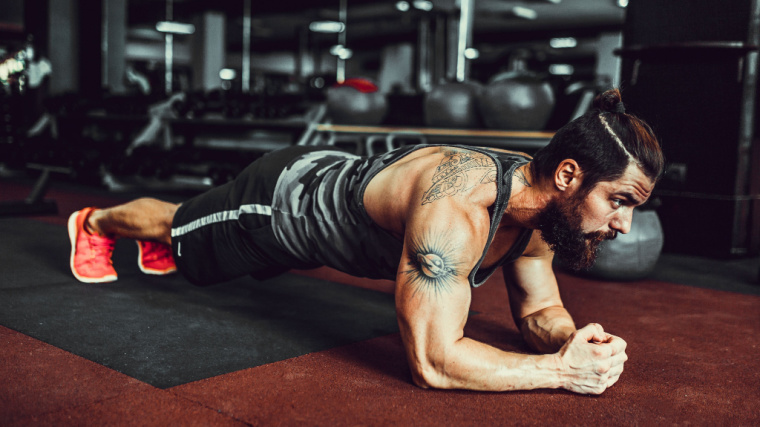 A person with tattoos on their arms holds a plank in the gym.