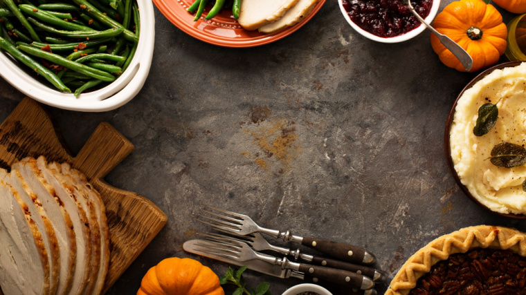 A table is laden with Thanksgiving plates and some utensils.