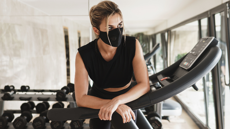 woman in mask rests on treadmill during workout
