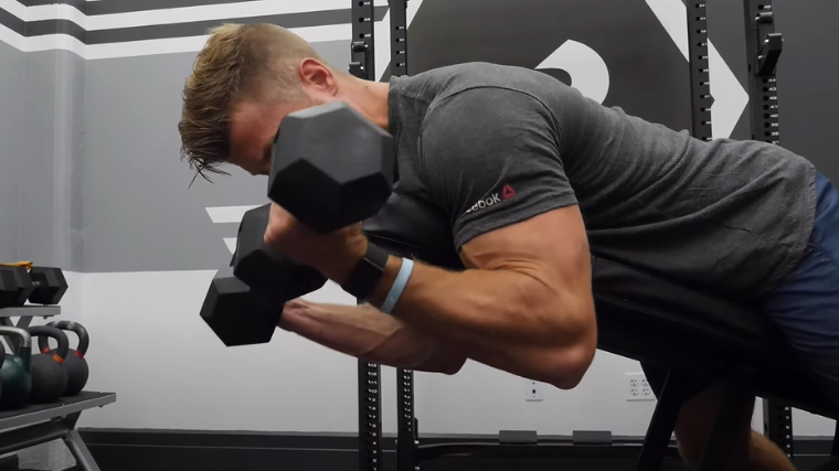 Man squeezes biceps hard at the top of spider curl exercise