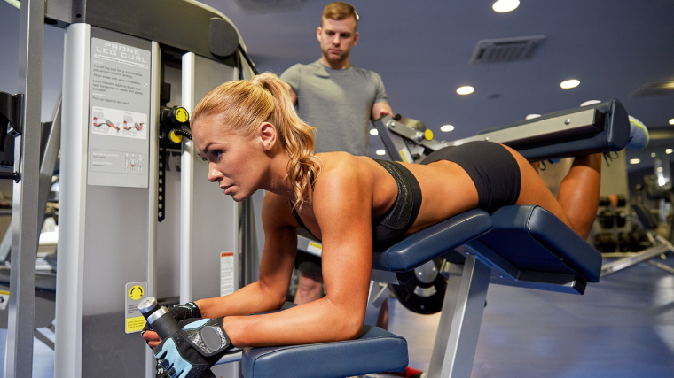 athlete in the gym working out leg curls while being coached