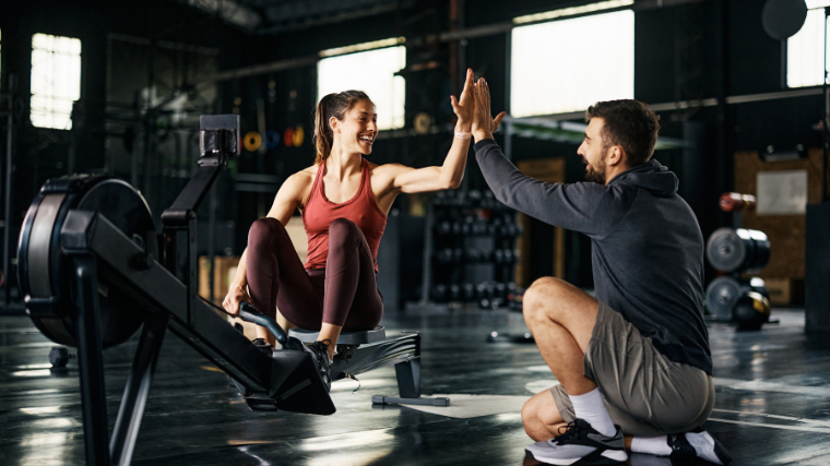 Athlete and coach in the gym doing a high five while athlete atop rowing machine.