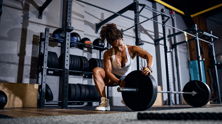 Athlete in gym preparing her barbell by loading it with plates.