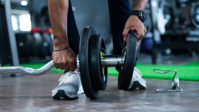 Bodybuilder loading plates onto a curved bar before lifiting it at the gym