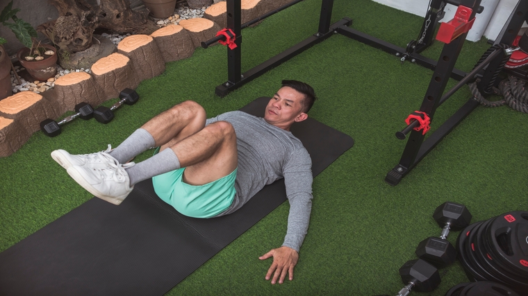 A person performs a reverse crunch on turf in a gym.