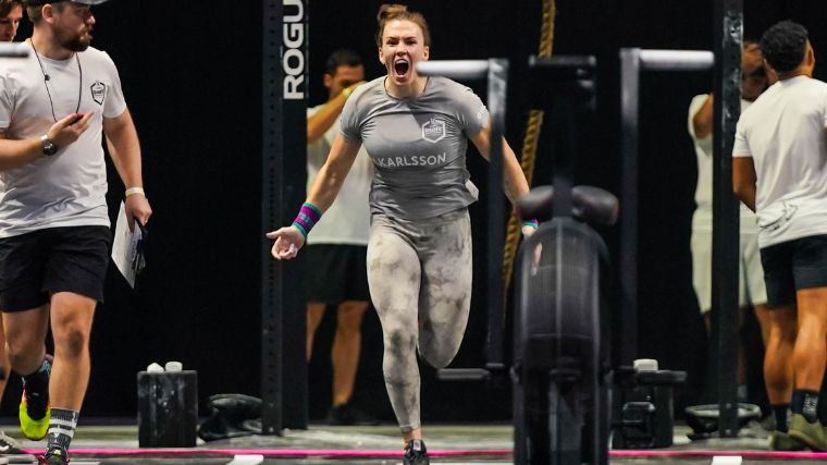 A woman sprints towards the camera wearing tan leggings and a grey shirt. 