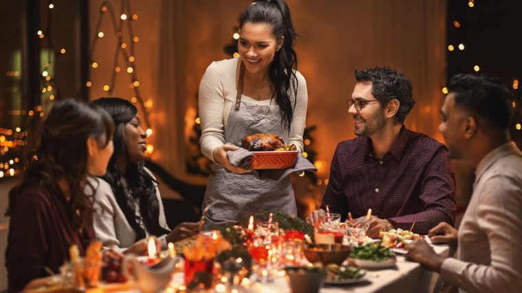 A group of people sitting at the dinner table with one person serving a plate of meat.