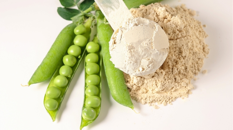 Peas beside a scoop of plant-based protein powder.