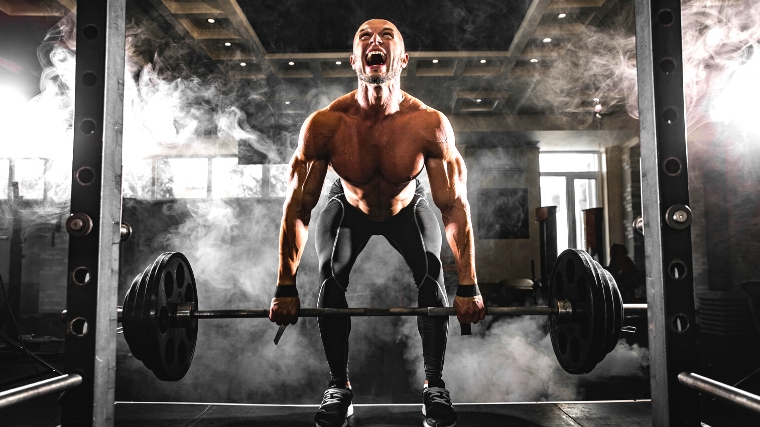 A shirtless person performing a deadlift in the gym.