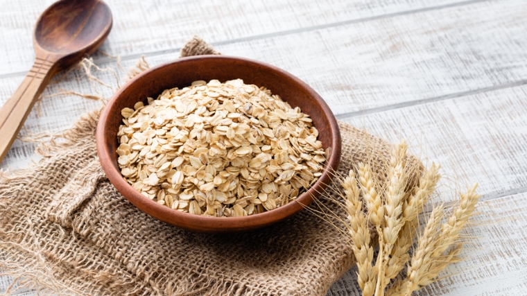 Oats in a wooden bowl beside a wooden spoon