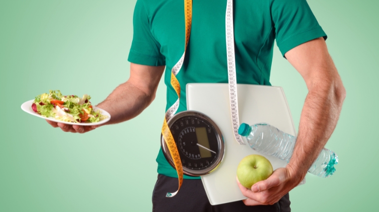 Person carrying a plate of salad in one hand and an apple and water on the other.