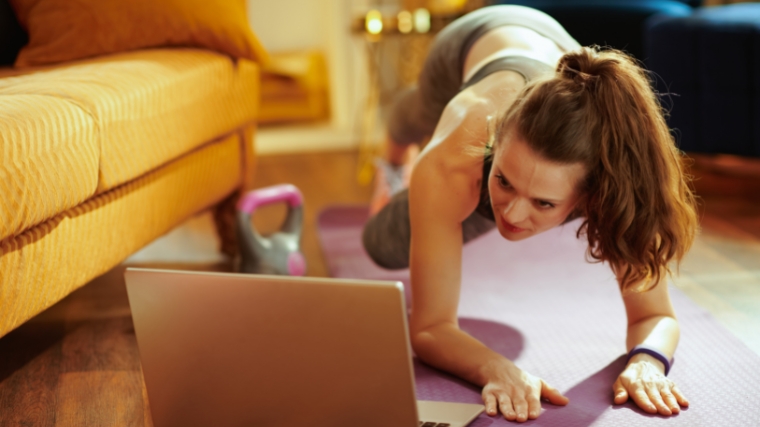 Person on a yoga mat following exercise moves on their laptop.