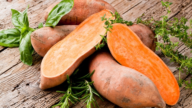 Whole and sliced orange sweet potatoes on wooden counter