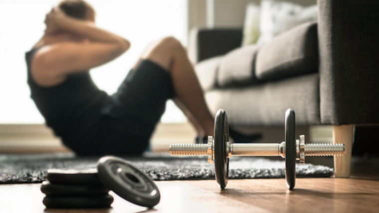 Man doing sit-ups at home with dumbbell in the foreground.