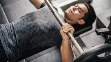 A person sets up to perform a barbell bench press with a pronated grip.