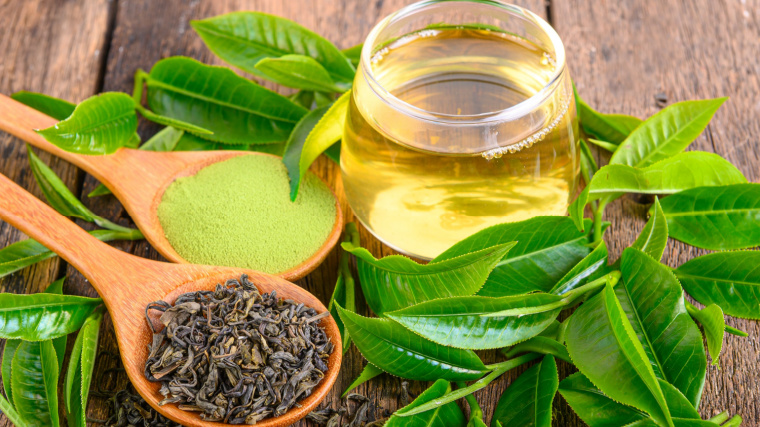 A clear jar of green tea sits amidst matcha powder and tea leaves.