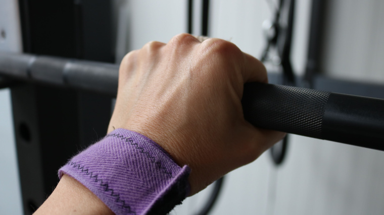 A person's hand grasps a barbell with a pronated grip.