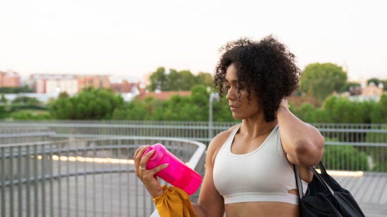 A person with curly hair shakes a protein shaker bottle on the go.