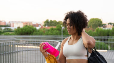 A person with curly hair shakes a protein shaker bottle on the go.