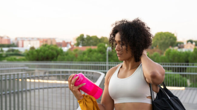 A person with curly hair shakes a protein shaker bottle on the go.