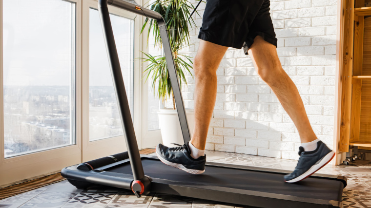 Person walking on compact treadmill overlooking city through window.