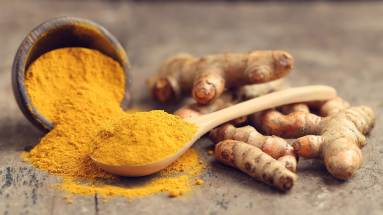 A bowl of turmeric powder with a wooden spoon sits on a table.