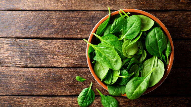 A wooden bowl of spinach sits on a wooden table.