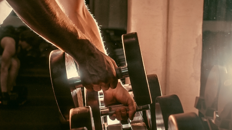 hands removing dumbbells from rack in sunny gym 