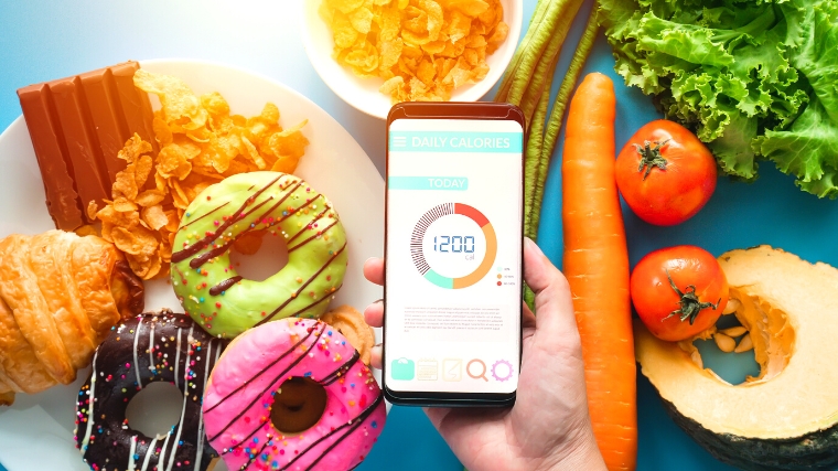 Person checking a calorie calculator app comparing pastries and vegetables.