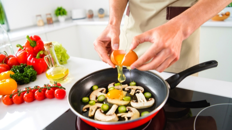 Person cooking mushrooms and egg in a frying pan.