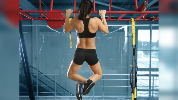 Foto de Sporty fitness couple doing pull up on horizontal bar in gym.  Muscular man and woman pulling up, working out. do Stock