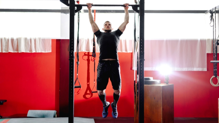 Person in back shorts and shirt performing a pull up.