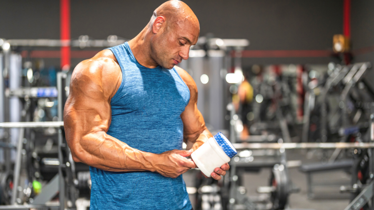 A bodybuilder holding a container of pre-workout protein powder.