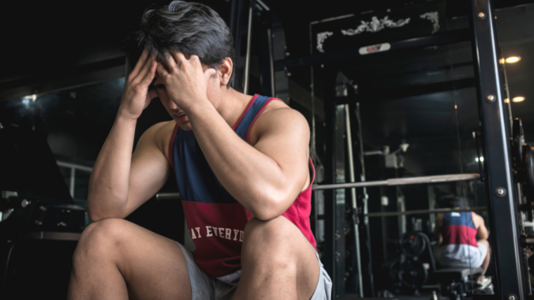 A frustrated or sleepy gymgoer with his face in his hands.