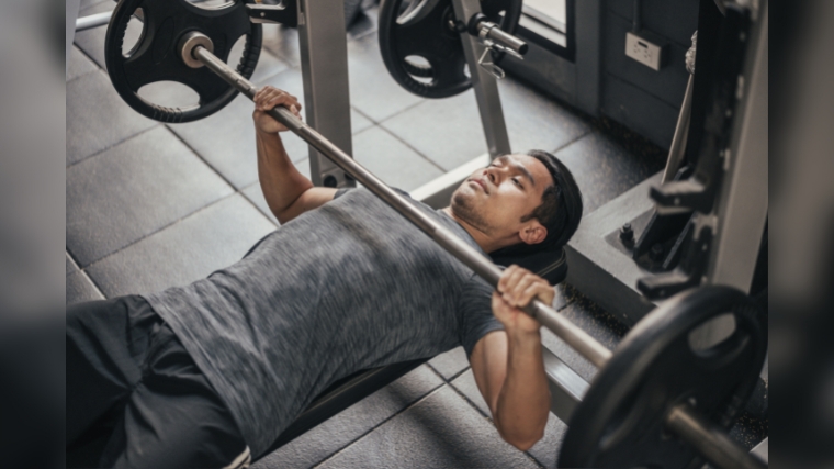 A person lowering the barbell to his chest on the bench.