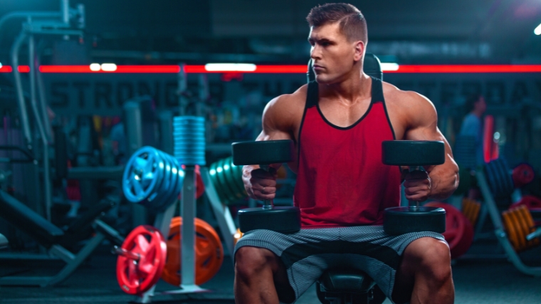 Bodybuilder with dumbbells sitting in the gym.