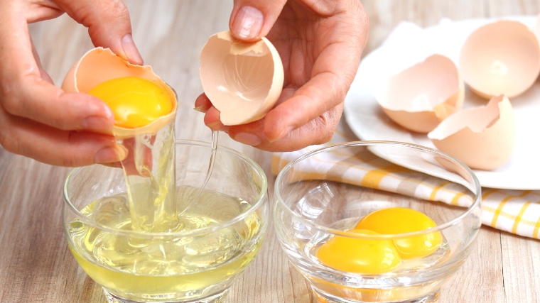 Egg whites being separated from egg yolks., in separate transparent bowls.