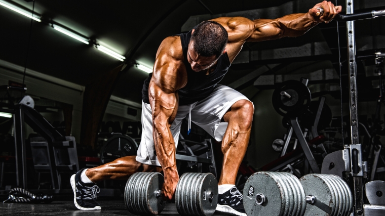 Muscular bodybuilder ready to lift a dumbbell off the floor.