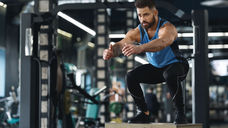 A person performs a box jump in the gym.