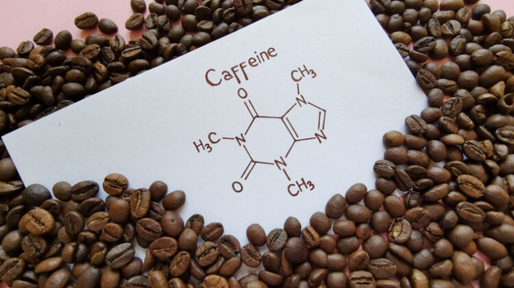 Caffeine chemical symbol on white paper partially tucked under a pile of coffee beans