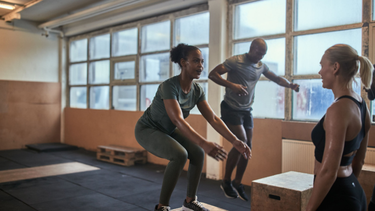 Two athletes perform box jumps while a coach looks on.