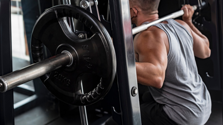 Person in grey tank top squatting in a smith machine