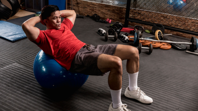 A person performs a sit-up on a stability ball in the gym.