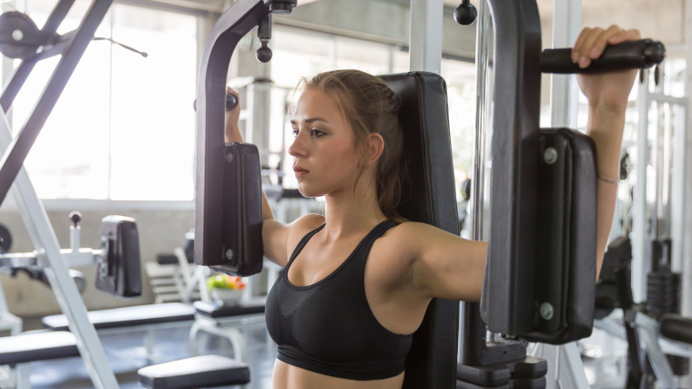 Woman performs chest flyes on pec deck machine in gym 