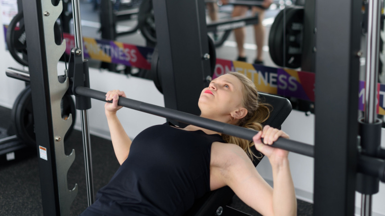 Person bench pressing in a smith machine in a black tank top